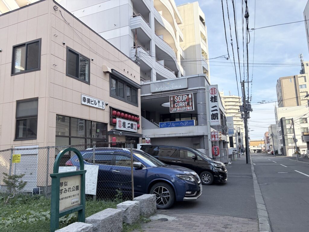 琴似すみれ公園の案内板と、車が停まる店舗周辺の通り