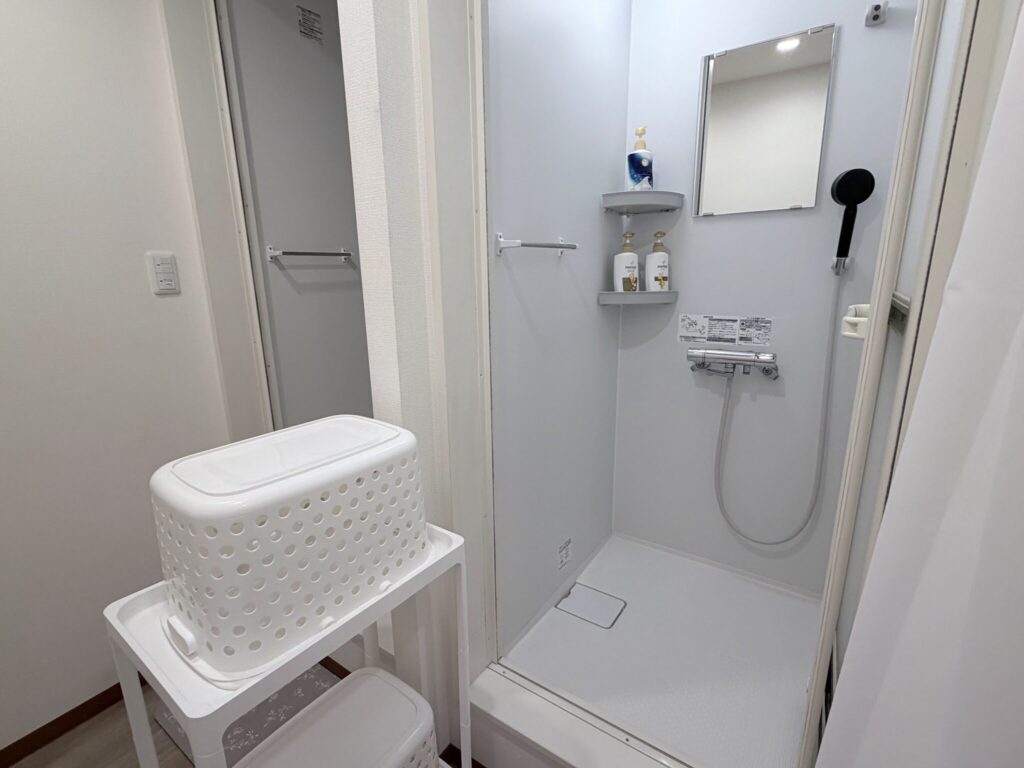 シャンプー類が置かれた個室のシャワー室と、手前の脱衣かごの置かれた棚