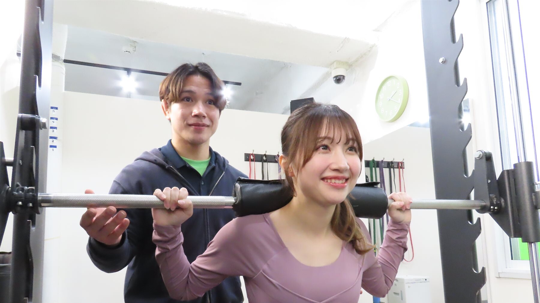 トレーナーの補助でバーベルスクワットをする女性
